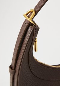 Borsa a mano in pelle marrone con finitura testurizzata, hardware dorato, dettagli con zip e una singola tracolla regolabile. Presenta una silhouette curvata.