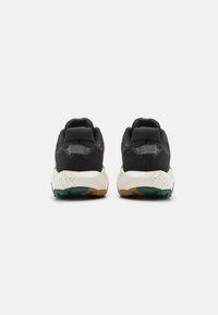 Zapatos deportivos negros con una parte superior de tela texturizada, una entresuela blanca acolchada con motas y una suela de goma con acentos verdes.