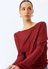 Langärmliges Oberteil in tiefem Rot, aus einem leichten, leicht durchsichtigen Stoff. Verfügt über einen lässigen Schnitt und ein Off-Shoulder-Design mit einer glatten Textur.