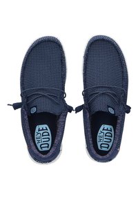 Baskets à enfiler bleu marine avec une tige en textile texturé, des lacets élastiques et une semelle blanche mouchetée. Présente une étiquette intérieure bleue.