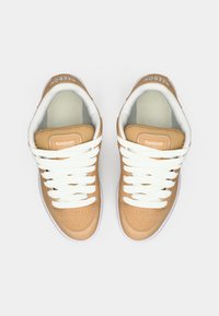 Sneakers in pelle color tan con lacci bianchi e suole in gomma. Il design presenta perforazioni sulla punta e un marchio sulla linguetta.