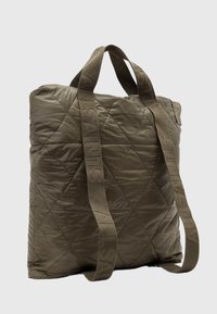 Prošívaná taška v olivově zelené barvě, vyrobená z robustní látky, s širokými popruhy s raženým logem a čtvercov�ým tvarem.