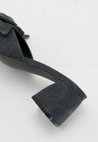 Zoccolo in denim con punta arrotondata e tacco a blocco largo. Colore grigio scuro con superficie texturizzata e leggera lucentezza ai bordi.