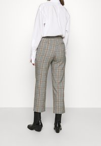 Grå och brun rutig byxa med avslappnad passform, hög midja och kort längd, tillsammans med svarta ankelskors. Vit skjorta bärs urstoppad.