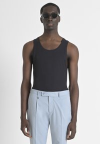 Top negro de tirantes con textura acanalada, combinado con pantalones plisados de un tono azul claro. El modelo lleva gafas de sol oscuras. Diseño simple y limpio.