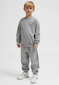 Grå sweatshirt och joggingbyxor som är gjorda av mjukt fleece-material. Båda har ribbade muddar och en liten logotyp broderad på bröstet och på benet.