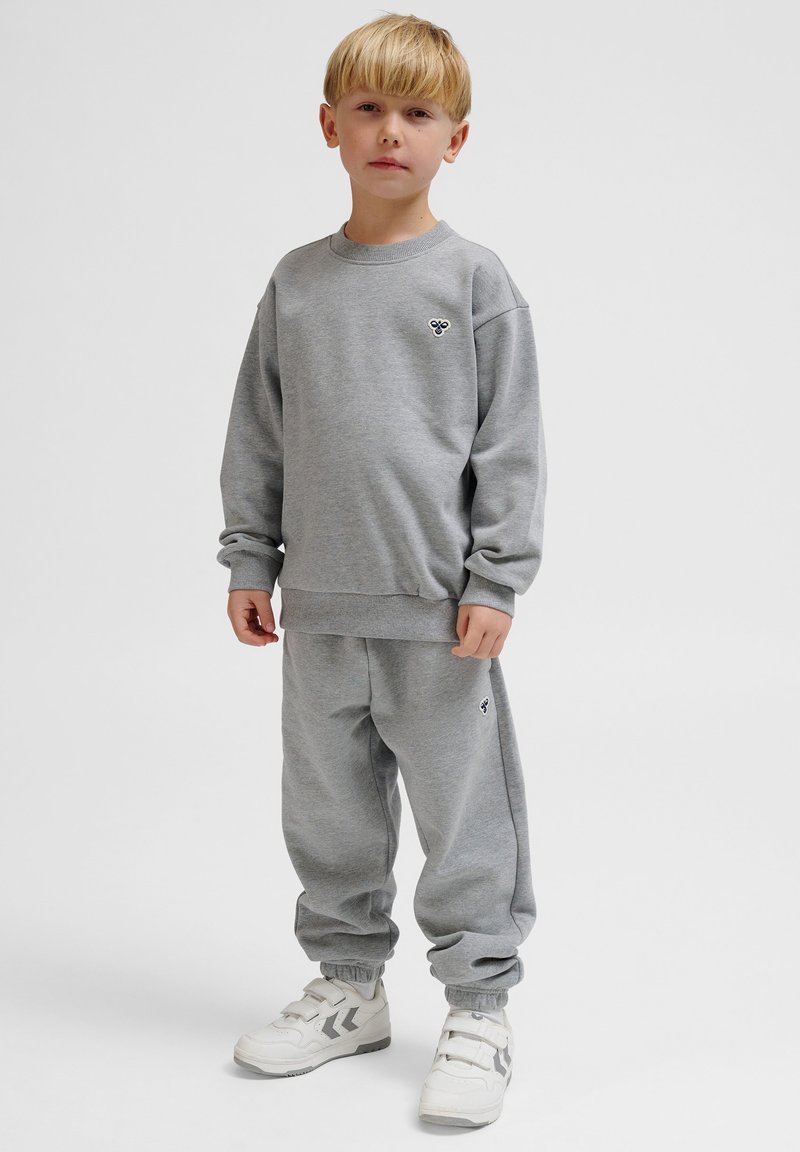 Grå sweatshirt och joggingbyxor som är gjorda av mjukt fleece-material. Båda har ribbade muddar och en liten logotyp broderad på bröstet och på benet.