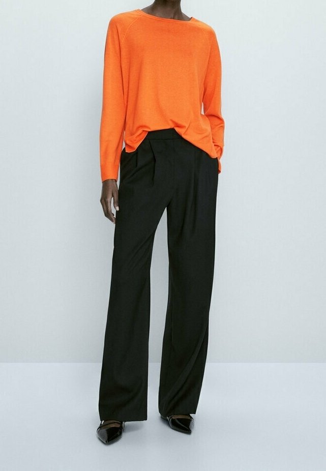 Oranges Langarmoberteil mit weitem Ausschnitt, kombiniert mit schwarzen weiten Hosen und spitzen schwarzen Ballerinas. Einfaches, klares Design.