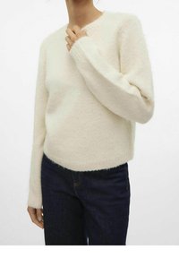 Hellbeige, fuzziger Pullover mit rundem Ausschnitt und langen Ärmeln, kombiniert mit dunkelblauen Jeans. Weicher Stoff und lockere Passform.