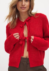 Rote Strickjacke mit strukturiertem Finish, langen Ärmeln, Rundhalsausschnitt und einer Bindeschließe vorne.
