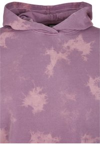 Fialová mikina vyrobená z mäkkej látky s motívom tie-dye v svetlejších odtieňoch. Má voľnú kapucňu a prešité švy.