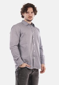 Camicia button-up in tessuto stampato, con un motivo geometrico blu navy e bianco, con maniche lunghe e colletto a punta. Pantaloni grigi.