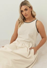 Hame säännär, jossa on musta reunus, kerätty vyötärö ja sivutaskut. Valmistettu kevyestä kankaasta, jolla on sileä rakenne.