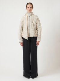Světlá béžová prošívaná bunda s vysokým límcem a zipem, doplněná o odpovídající šálu; doplněná černými kalhotami s širokými nohavicemi. Hladká textura.