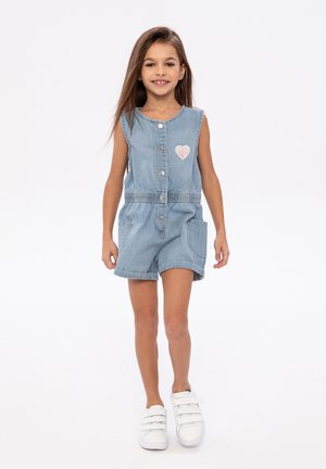Romper en denim bleu clair avec design sans manches, boutons sur le devant, taille élastique et détail en forme de cœur. Assorti avec des baskets blanches.