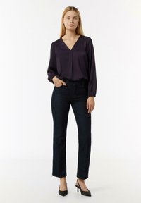 Dunkellila Bluse mit langen Ärmeln und V-Ausschnitt, kombiniert mit hochtaillierten, dunkelblauen Jeans und schwarzen spitzen High Heels. Einfaches, elegantes Design.