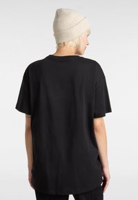 Sort bomulds T-shirt med løst fit og korte ærmer, der har en rund hals og et vævet label ved sidekant, set fra ryggen.