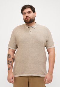 Polo beige en tricot texturé, avec un col et une patte de boutonnage à trois boutons. Manches courtes avec des détails au niveau des poignets.