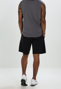 Haut gris sans manches et short noir à texture lisse. Chaussures de sport blanches avec des accents noirs. Tatouages visibles sur les bras.