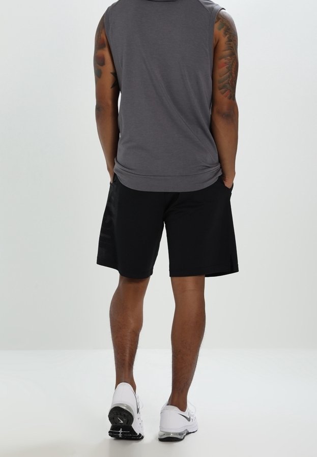 Haut gris sans manches et short noir à texture lisse. Chaussures de sport blanches avec des accents noirs. Tatouages visibles sur les bras.