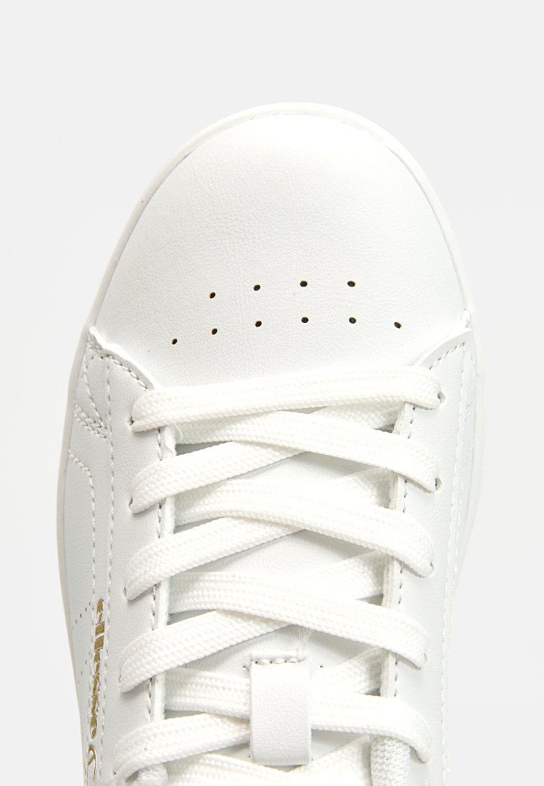 Baskets blanches avec un dessus en cuir lisse, bout rond et détails perforés. Dotées de lacets blancs et d'un subtil accent doré.