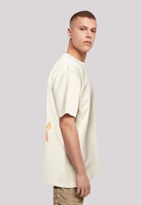 Off-white oversized cotton T-shirt with short sleeves, featuring a playful orange graphic on the back and ribbed neckline.