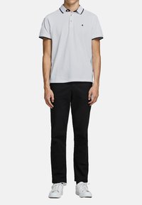 Hvid polo-shirt med sort krave og detaljer, parret med sorte bukser og hvide sneakers. Glat tekstur, klassisk lige pasform design.