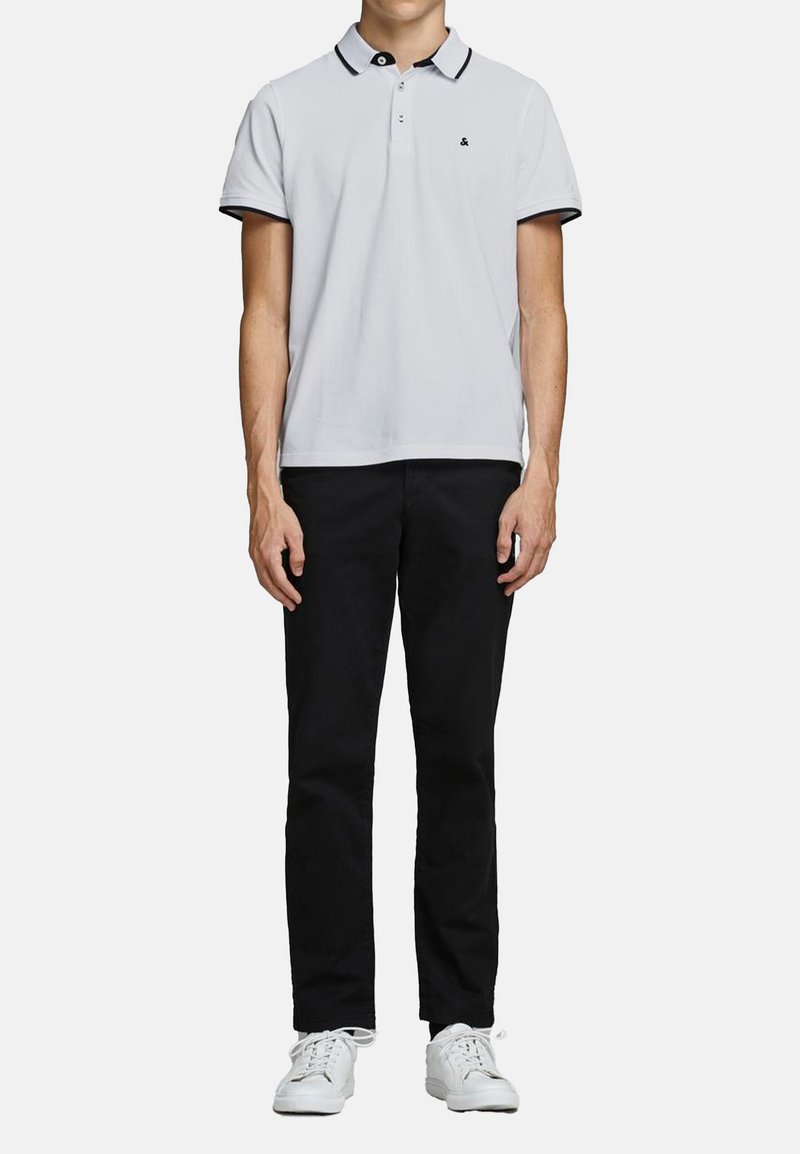 Polo bianco con colletto e dettagli neri, abbinato a pantaloni neri e sneakers bianche. Tessuto liscio, design classico a vestibilità dritta.