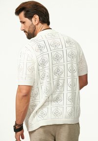 Weißer, kurzärmeliger Strickpullover mit einem Lochmuster und geometrischen Designs. Der strukturierte Stoff verbessert die Atmungsaktivität und den Komfort.