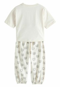 Ensemble en coton deux pièces comprenant un haut à manches courtes de couleur crème clair et un pantalon blanc avec des motifs de cœurs noirs et des poignets élastiques.