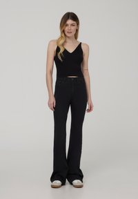 Top corto a coste nero con scollatura a V, abbinato a jeans neri a vita alta e a zampa. Il modello indossa sneaker bianche con dettagli beige.