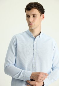 Camicia azzurra a maniche lunghe con bottoni, caratterizzata da un motivo testurizzato, colletto con bottoni e polsini con un solo bottone.