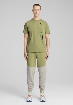 Oliven grøn træningstop med korte ærmer og en lynlås lomme, parret med lysegrå joggers med farveblokeret design og ribbede manchetter.