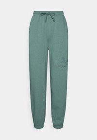 Joggingbyxor i dämpad teal, tillverkade av mjukt tyg. Har ett elastiskt midjeband med dragsko, smalnade ben och en logotyp patch på vänster lår.