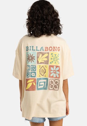 Cream oversized t-shirt featuring a colorful, block-patterned design with floral motifs and the text "BILLABONG" in bold, contrasting colors.