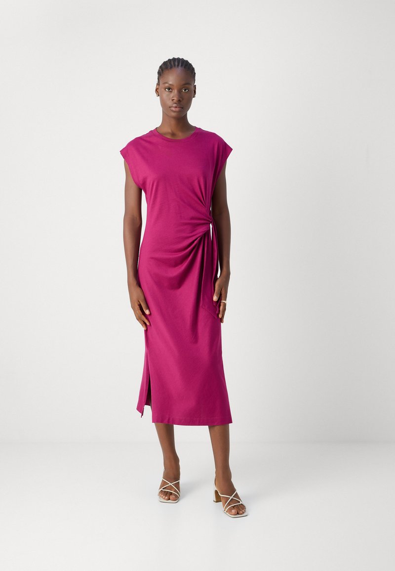 Fuchsia Midi-Kleid mit kurzen Ärmeln, seitlichem Raffungselement und einem Schlitz am Saum. Model trägt beigefarbene Absatzsandalen.