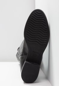 Stivale in pelle nera con suola in gomma testurizzata caratterizzata da motivi ondulati e fori di ventilazione. Accenti laterali con dettagli di cucitura minimi.