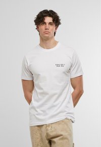 Hvid bomulds t-shirt med korte ærmer, rund halsudskæring og en trykt tekst "I dag var en god dag" i sort på venstre brystområde.