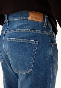 Jeans aus Denim in Mittelblau mit glatter Textur, geradem Schnitt und einem Lederpatch mit der Aufschrift "OSCAR JACOBSON" am Bund.