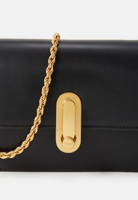 Bolsa de couro preta com uma alça de corrente dourada. Apresenta um formato retangular e um fecho de hardware dourado proeminente na frente.