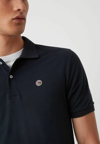 Tumesinine polo särk tekstuuriga kangast, klassikalise kraega ja väikese ümmarguse logo aktsendiga. Kaks nööpaukku.