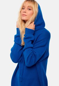 Blaue Strick-Hoodie mit lockerer Passform, langen Ärmeln und Kapuze mit Kordelzug. Die Textur ist weich und verfügt über gerippte Akzente an den Bündchen.