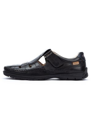 Zapato casual de cuero negro con detalles recortados, costuras texturizadas, correa ajustable y suela de goma para tracción. Diseño de perfil bajo.