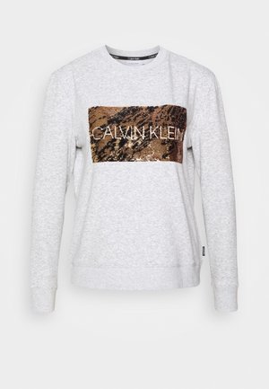Světle šedá mikina vyrobená z bavlněné směsi, s kovovým bronzovým flitrovým obdélníkovým potiskem s nápisem "CALVIN KLEIN" bílým textem. Standardní střih.