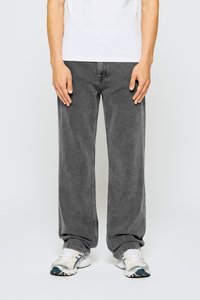 Jeans grises de pierna ancha con un acabado deslavado, hechos de denim. Combinados con zapatillas deportivas blancas y grises. El modelo lleva una camiseta blanca básica.