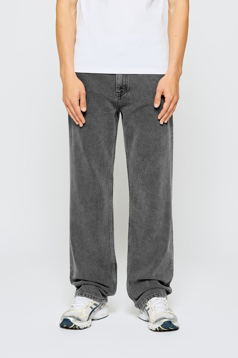 Jeans grises de pierna ancha con un acabado deslavado, hechos de denim. Combinados con zapatillas deportivas blancas y grises. El modelo lleva una camiseta blanca básica.