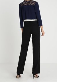 Marinblå kort topp med spetsdetaljer på ryggen, ihop med svarta byxor och högklackade skor. Slät textur, skräddarsydd passform.