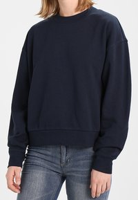 Sweat-shirt bleu marine, col rond, manches longues, ourlet court, tissu doux, design minimaliste, sans logo ni motif visible.