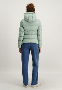 Mintgroene pufferjack met een capuchon, met een gequilte uitstraling. Gecombineerd met ruime blauwe spijkerbroeken en witte sneakers.