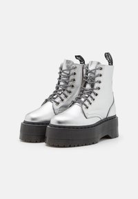 Botines metálicos plateados con una plataforma negra gruesa, que cuentan con un diseño de cordones, herrajes plateados y una pestaña en el talón.